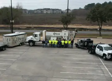 Workers in reflective vests beside trucks in parking lot.
