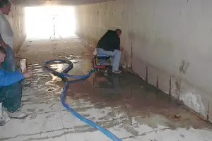 Workers using equipment in underground concrete tunnel.
