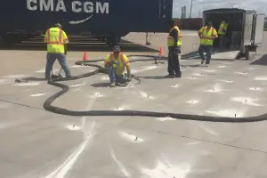Workers managing hoses at industrial shipping yard.