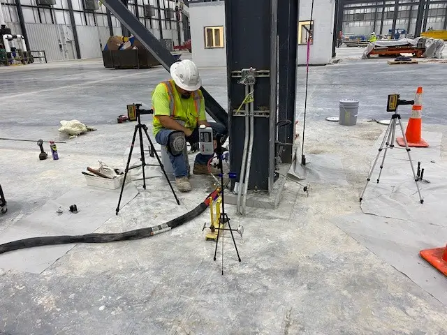 Worker using survey equipment at industrial construction site.