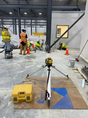 Construction workers using equipment at indoor site.
