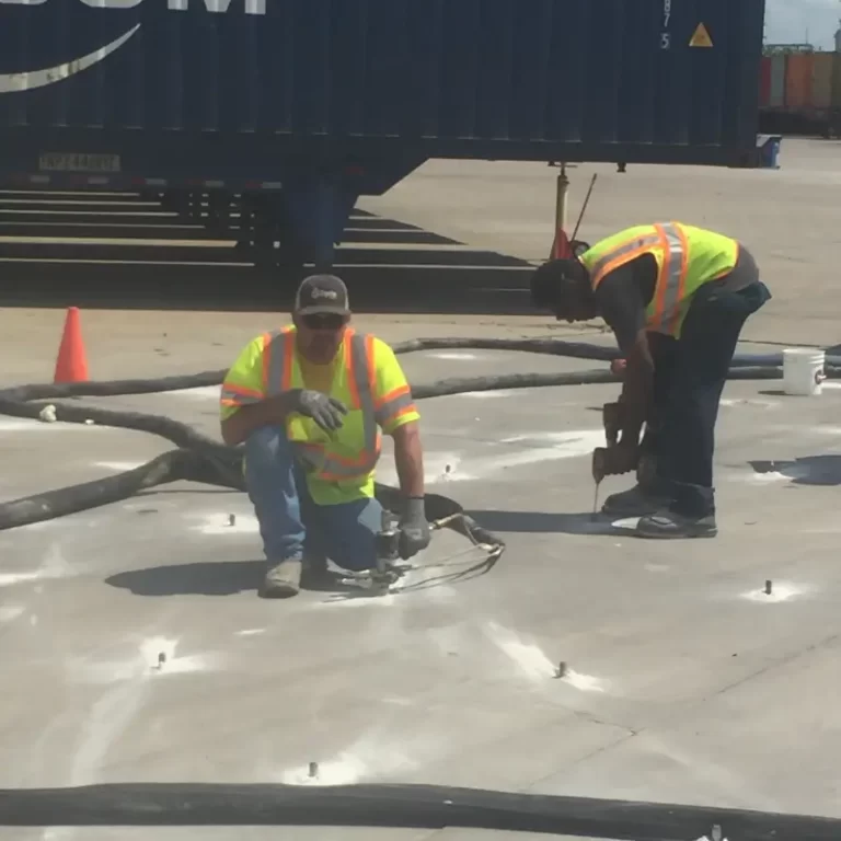 Workers in hi-vis repairing warehouse floor with tools.